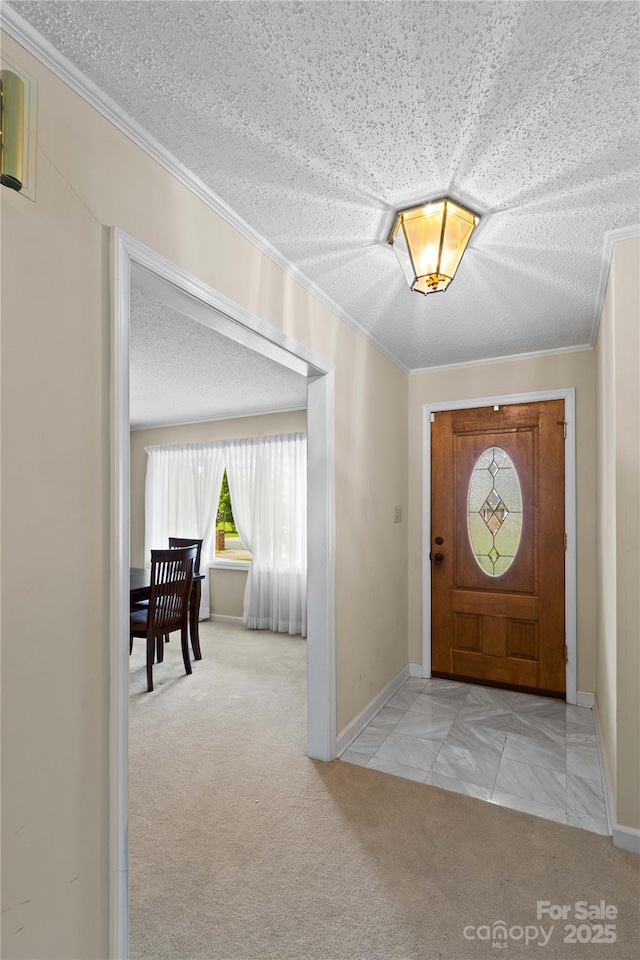 carpeted foyer entrance featuring a textured ceiling, baseboards, and ornamental molding