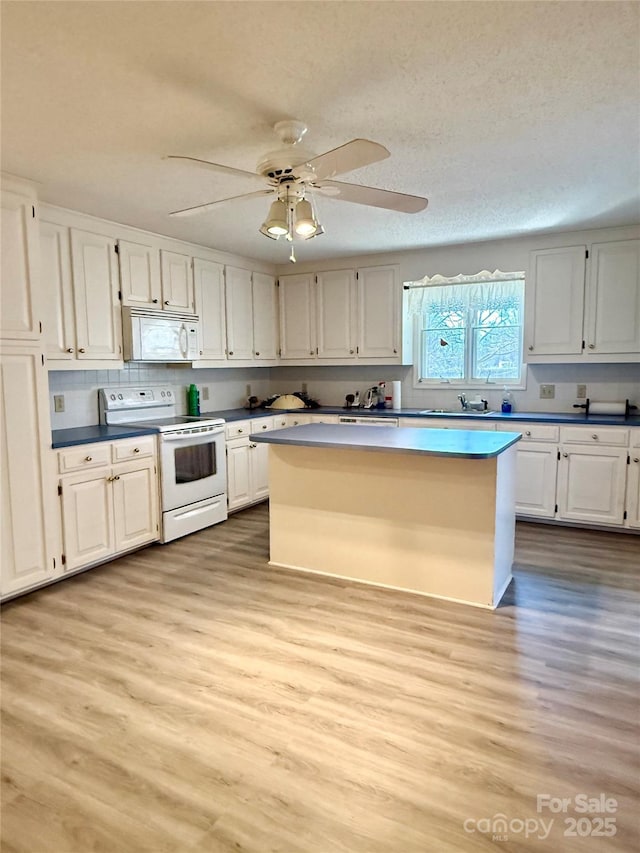 kitchen with white appliances, a kitchen island, white cabinets, a textured ceiling, and light wood-type flooring