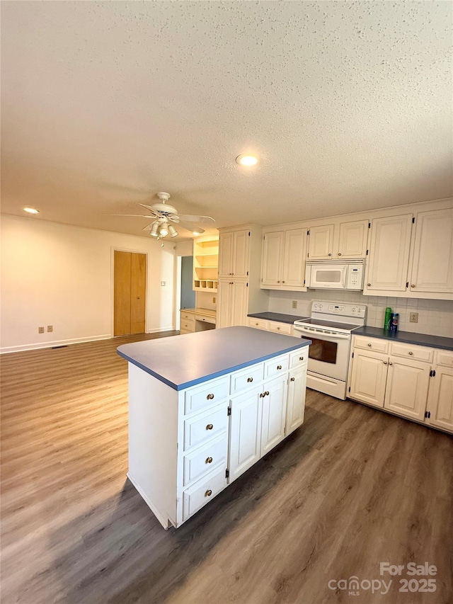 kitchen with dark countertops, a kitchen island, white appliances, white cabinetry, and dark wood-style flooring