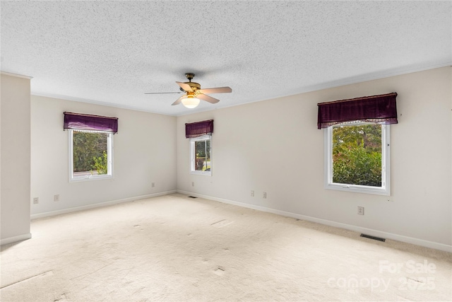 carpeted spare room with plenty of natural light, baseboards, visible vents, and a textured ceiling