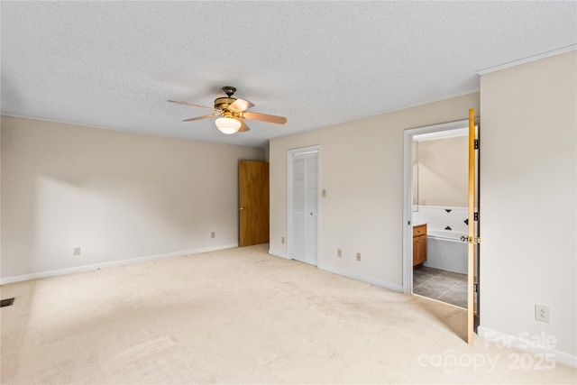 unfurnished bedroom with ceiling fan, baseboards, light carpet, ensuite bath, and a textured ceiling