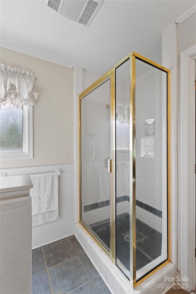 full bathroom with tile patterned flooring, tile walls, a wainscoted wall, a stall shower, and a textured ceiling