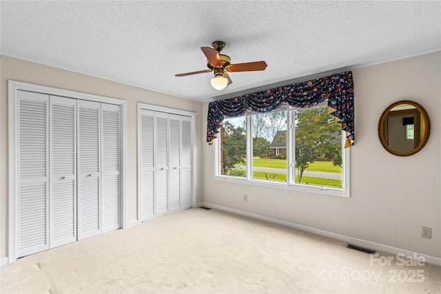 unfurnished bedroom with carpet, visible vents, two closets, and a textured ceiling