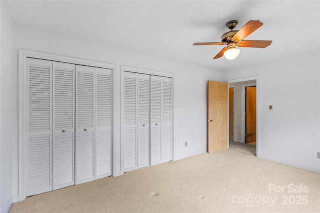 unfurnished bedroom with baseboards, ceiling fan, multiple closets, a textured ceiling, and light carpet