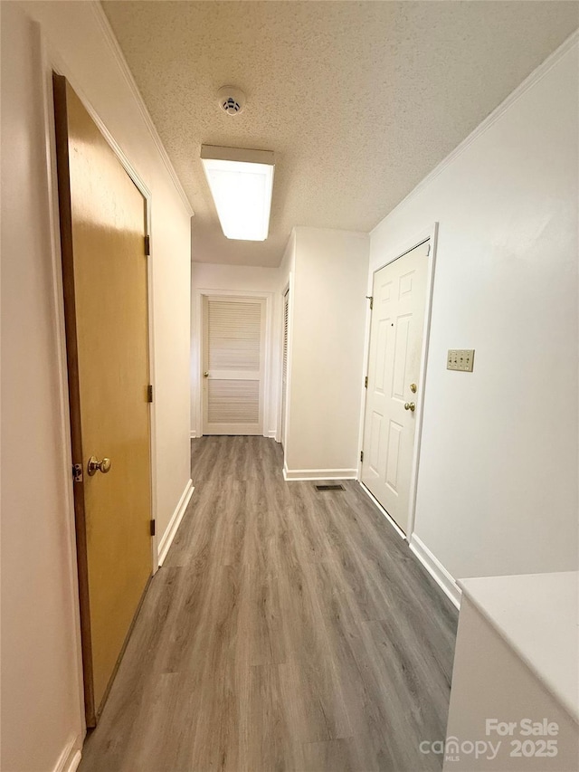 corridor with a textured ceiling, crown molding, baseboards, and wood finished floors