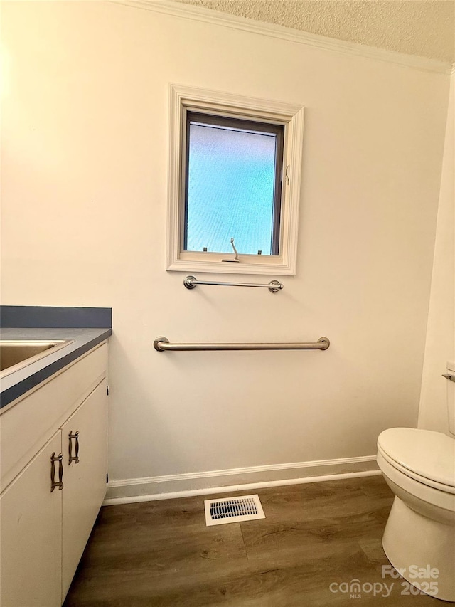 bathroom with vanity, wood finished floors, visible vents, baseboards, and toilet