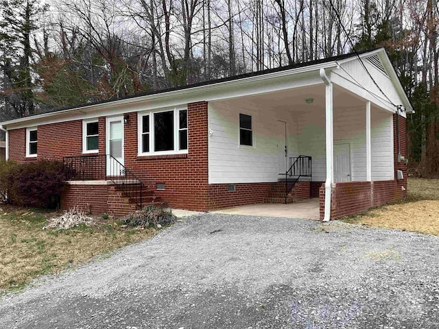 view of front of property with gravel driveway, brick siding, and crawl space