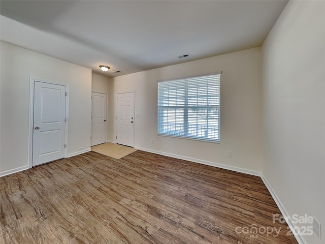 unfurnished room featuring visible vents, baseboards, and wood finished floors