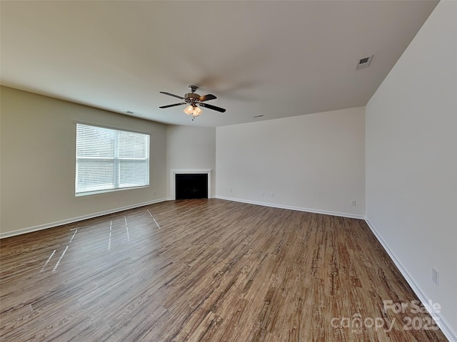 unfurnished living room with a ceiling fan, wood finished floors, visible vents, baseboards, and a fireplace