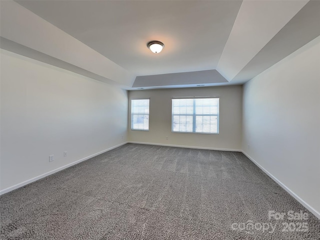 empty room featuring a raised ceiling, carpet flooring, and baseboards