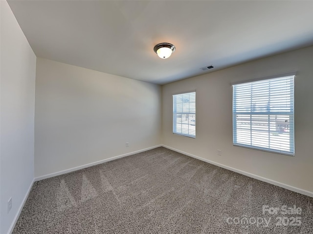 spare room with dark colored carpet, visible vents, and baseboards