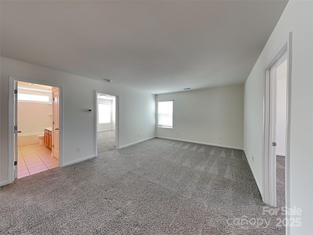 empty room with baseboards, light colored carpet, and light tile patterned flooring