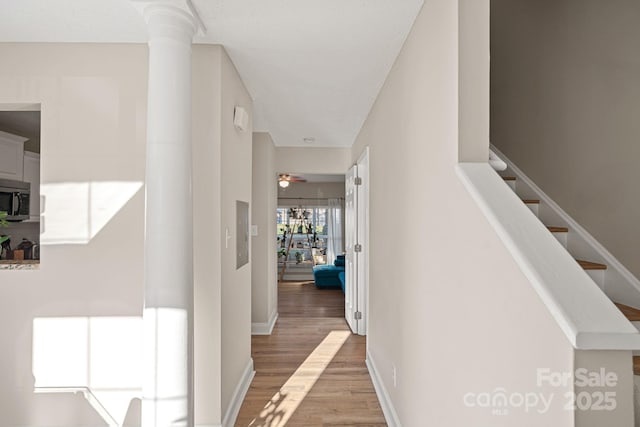 corridor featuring stairway, baseboards, light wood-type flooring, and ornate columns