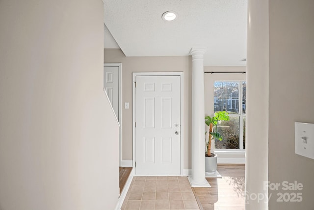 entryway with light tile patterned floors, decorative columns, baseboards, and a textured ceiling