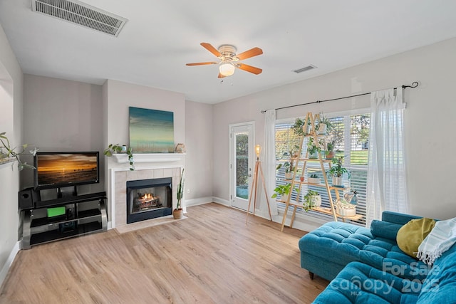 living area with a tiled fireplace, wood finished floors, visible vents, and baseboards