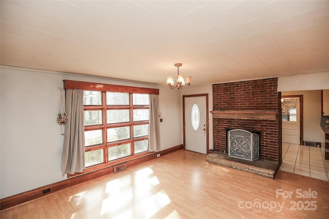 unfurnished living room with wood finished floors, baseboards, visible vents, a fireplace, and a chandelier