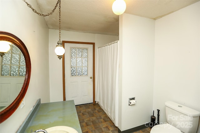 full bathroom with toilet, stone finish floor, a sink, a textured ceiling, and a shower with shower curtain