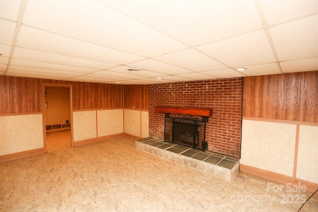 unfurnished living room with wooden walls, a fireplace, and a paneled ceiling