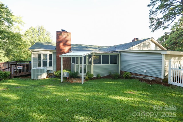 rear view of property featuring central air condition unit, a chimney, a yard, and a sunroom