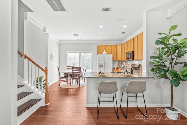 kitchen with stainless steel microwave, a peninsula, white refrigerator with ice dispenser, and visible vents