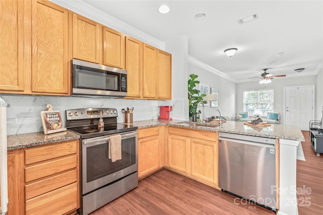 kitchen with visible vents, a peninsula, a sink, appliances with stainless steel finishes, and crown molding