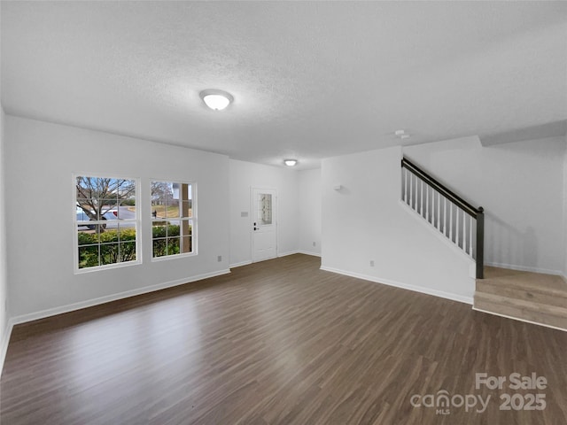 unfurnished living room featuring dark wood-style floors, stairway, a textured ceiling, and baseboards