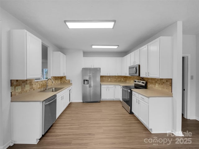 kitchen featuring light wood-style flooring, a sink, light countertops, appliances with stainless steel finishes, and white cabinetry