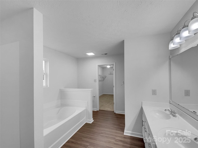 full bathroom featuring a textured ceiling, wood finished floors, baseboards, a bath, and vanity