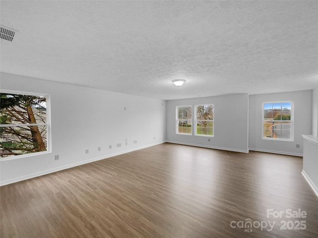 unfurnished living room with baseboards, plenty of natural light, dark wood-type flooring, and a textured ceiling