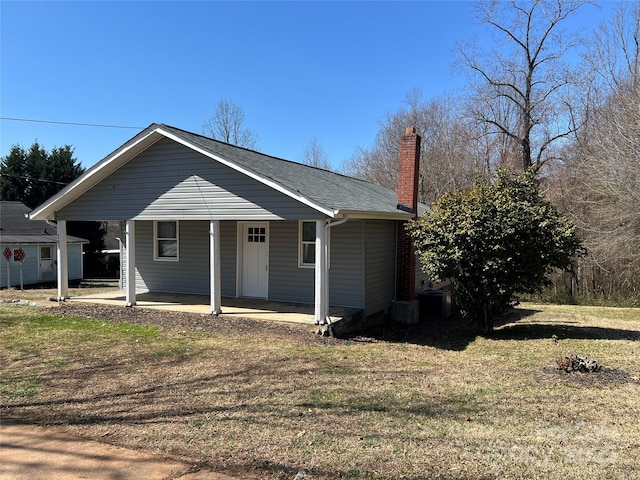 bungalow-style home with a carport, a porch, a chimney, and a front lawn