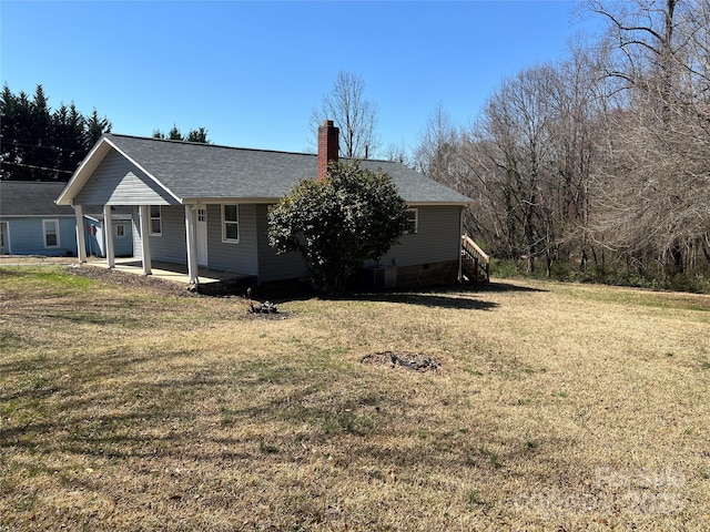 view of front facade with a shingled roof, a front lawn, and a chimney