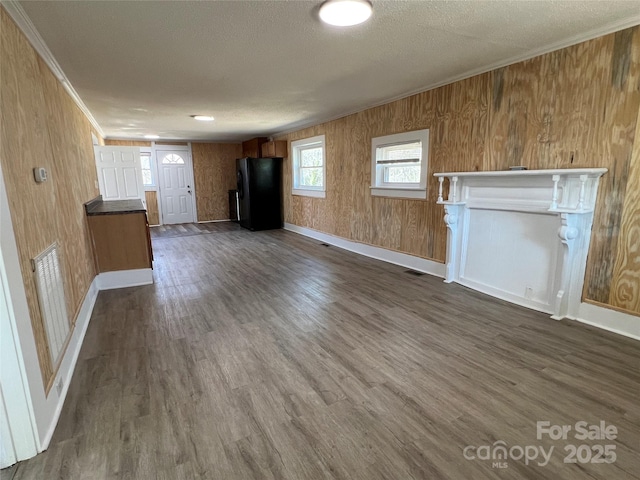 unfurnished living room featuring dark wood-style floors, a textured ceiling, visible vents, and ornamental molding