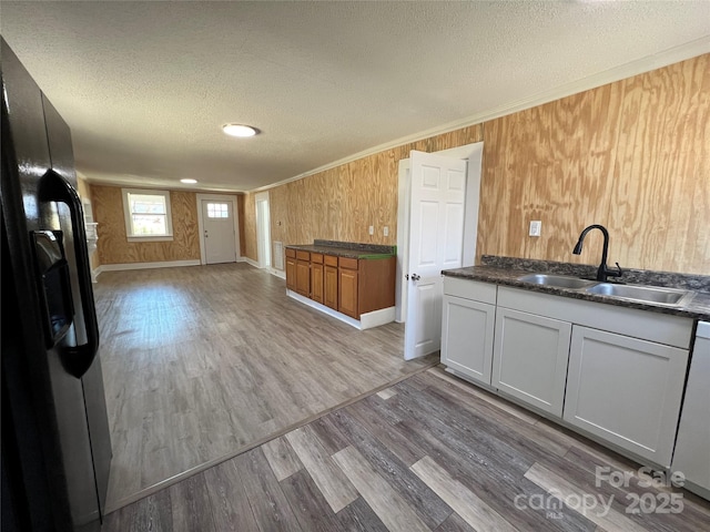 kitchen featuring wood finished floors, a sink, a textured ceiling, crown molding, and black refrigerator with ice dispenser