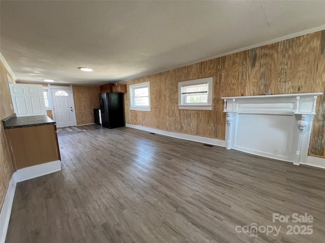 unfurnished living room with a textured ceiling, visible vents, dark wood-style flooring, and ornamental molding