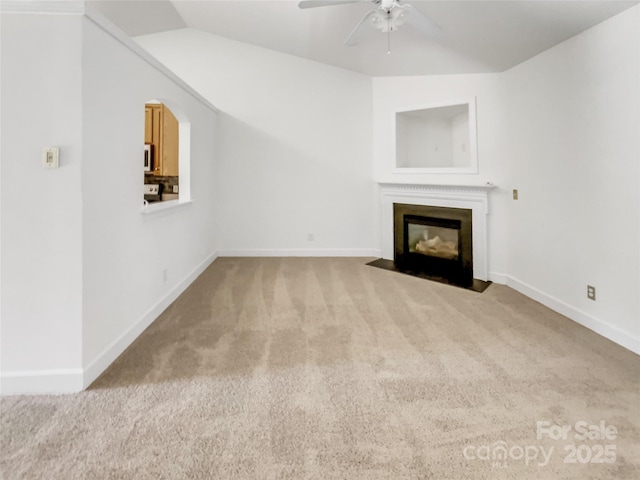 unfurnished living room with a fireplace with flush hearth, carpet, baseboards, and ceiling fan