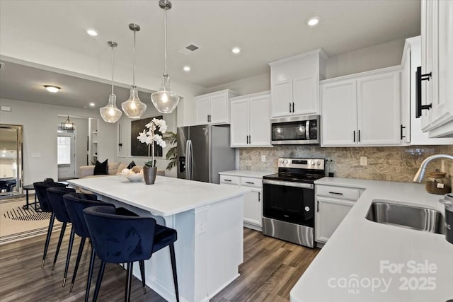 kitchen with a sink, appliances with stainless steel finishes, white cabinetry, tasteful backsplash, and a center island