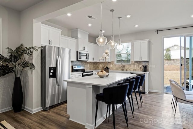 kitchen featuring dark wood-style floors, decorative backsplash, light countertops, appliances with stainless steel finishes, and a center island