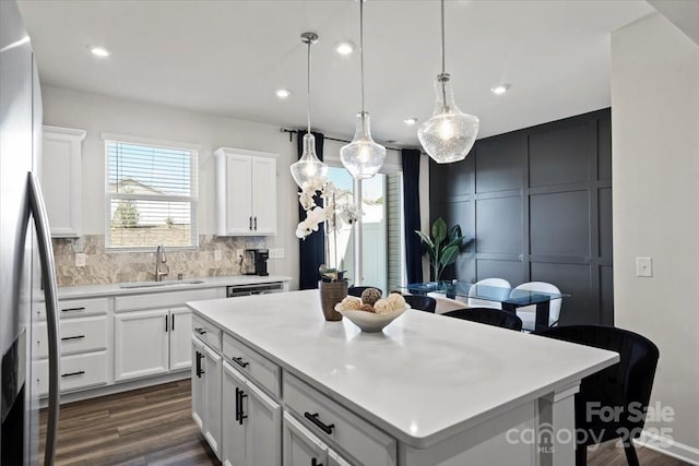 kitchen featuring stainless steel refrigerator with ice dispenser, a sink, a kitchen island, tasteful backsplash, and light countertops