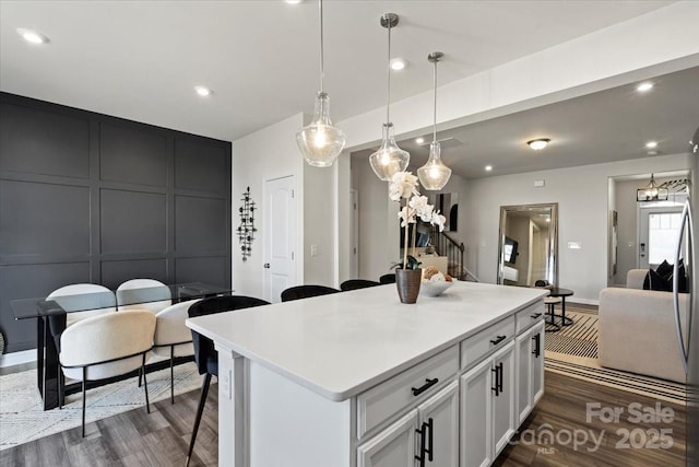 kitchen featuring a kitchen island, dark wood-style flooring, hanging light fixtures, light countertops, and a decorative wall