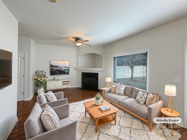 living area featuring a glass covered fireplace, wood finished floors, baseboards, and a ceiling fan