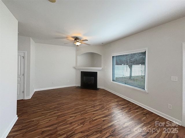 unfurnished living room with dark wood-type flooring, a fireplace with flush hearth, a ceiling fan, and baseboards