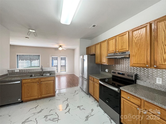 kitchen with tasteful backsplash, under cabinet range hood, brown cabinetry, stainless steel appliances, and a sink