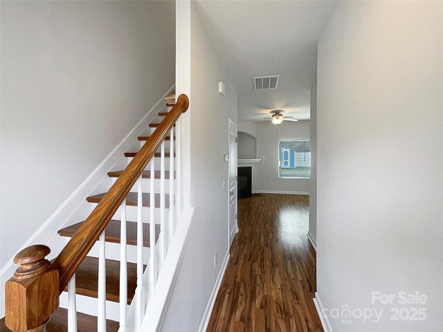 staircase featuring visible vents, wood finished floors, a fireplace, baseboards, and ceiling fan