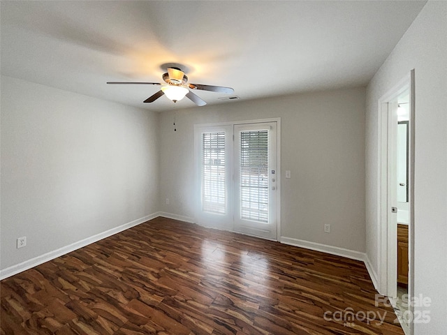 spare room with a ceiling fan, dark wood-style floors, visible vents, and baseboards