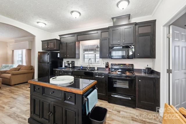 kitchen with light wood finished floors, ornamental molding, arched walkways, black appliances, and a sink