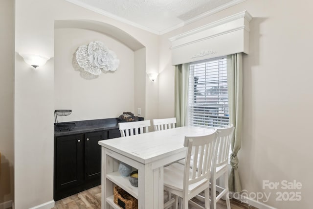 dining area featuring light wood-type flooring, baseboards, a textured ceiling, and crown molding