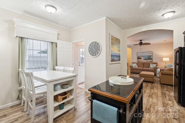 dining room with ceiling fan, ornamental molding, light wood-style floors, arched walkways, and a textured ceiling