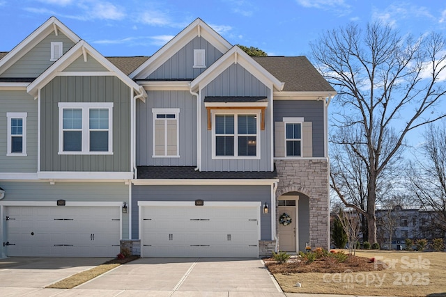 view of property with driveway, an attached garage, a shingled roof, stone siding, and board and batten siding