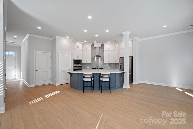 kitchen with a breakfast bar, white cabinetry, appliances with stainless steel finishes, wall chimney exhaust hood, and light countertops