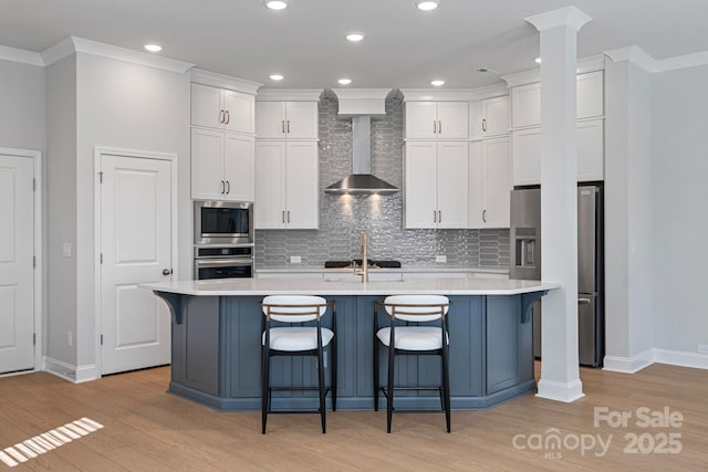 kitchen with backsplash, appliances with stainless steel finishes, wall chimney exhaust hood, white cabinets, and light countertops